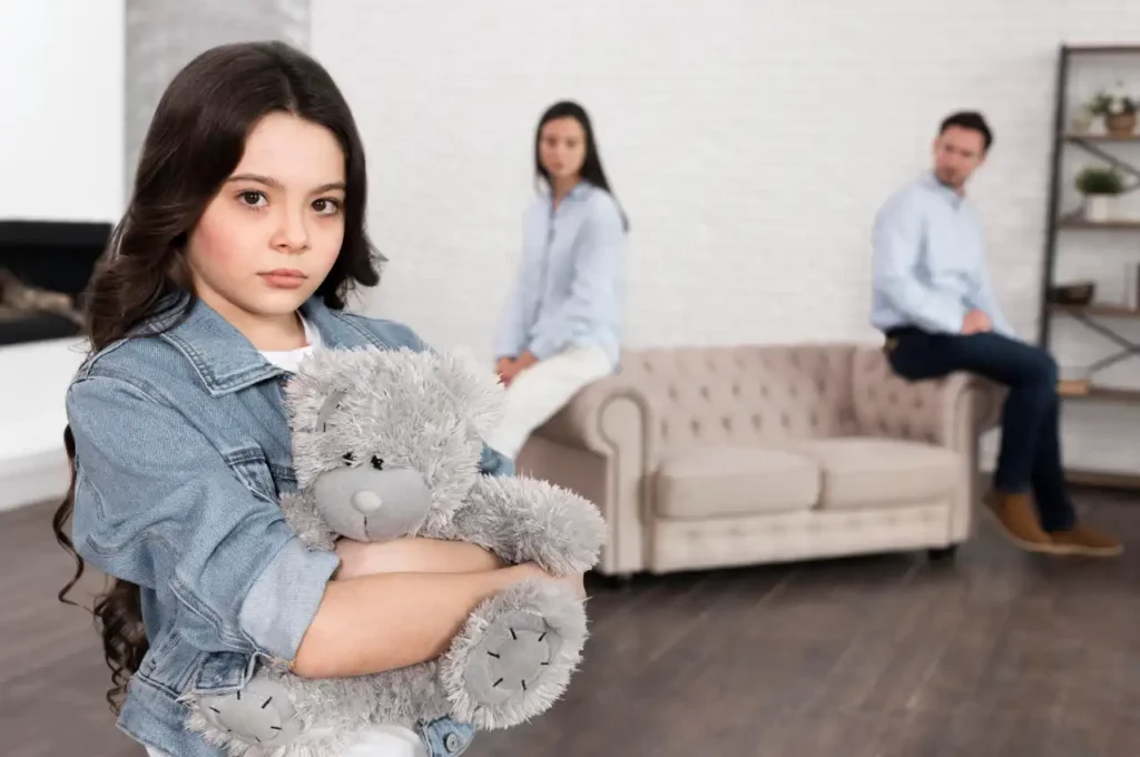 Couple sitting apart on a couch with a sad child holding a toy, representing child support and family separation.