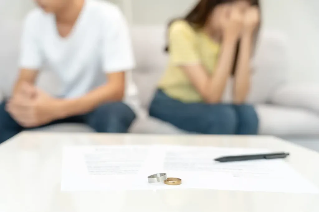 Sad couple sitting apart with documents and rings on the table, representing divorce.