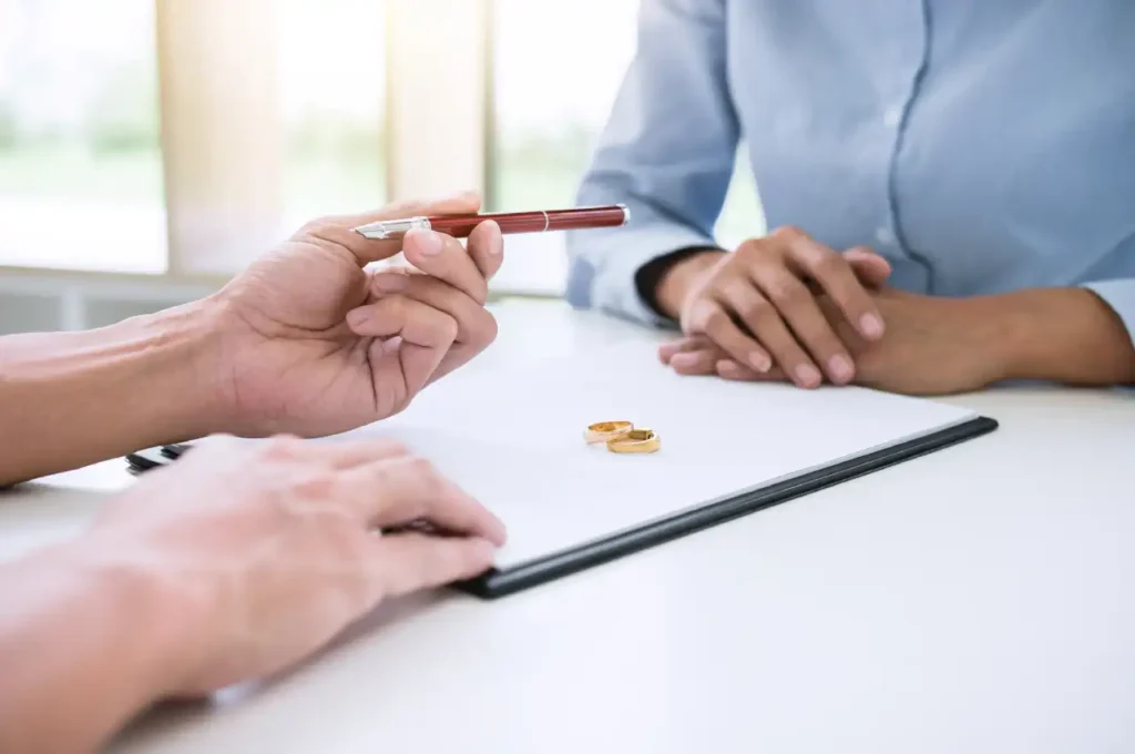 Two people sitting opposite each other at a table with documents and wedding rings, one holding a pen, representing spousal maintenance.