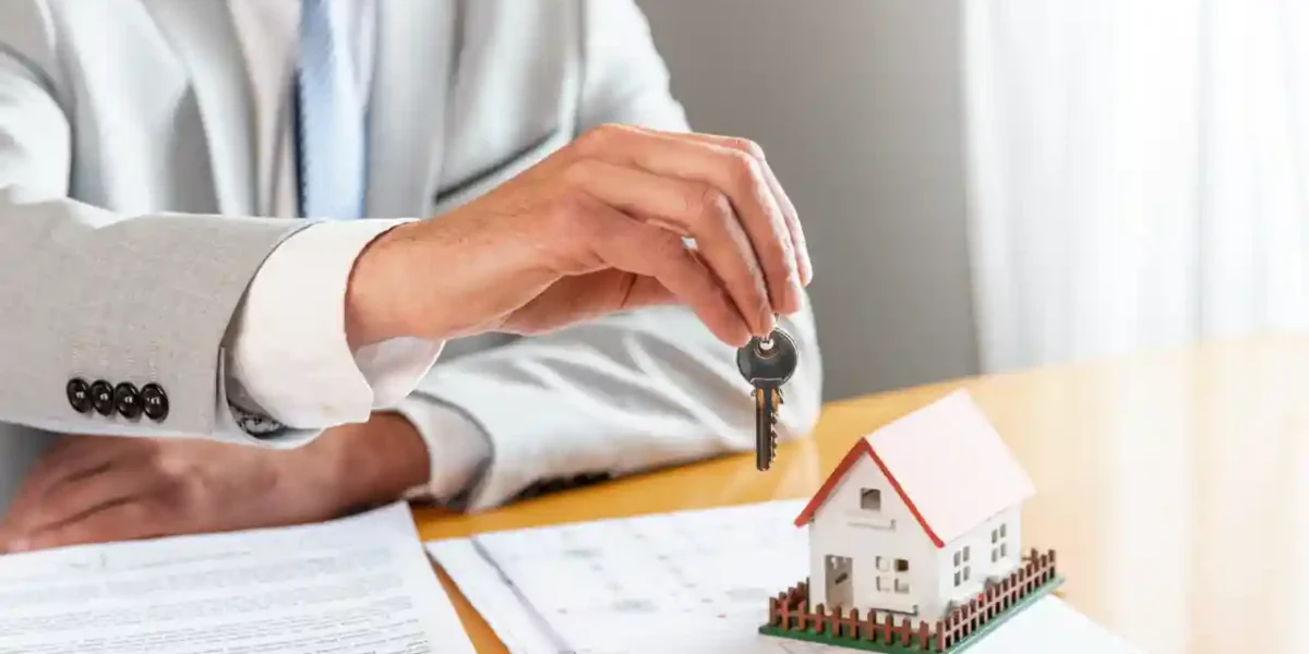 Man holding house keys with model home and documents representing successful conveyancing.