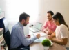 A couple is consulting with a lawyer while reviewing and discussing a legal agreement document in an office.