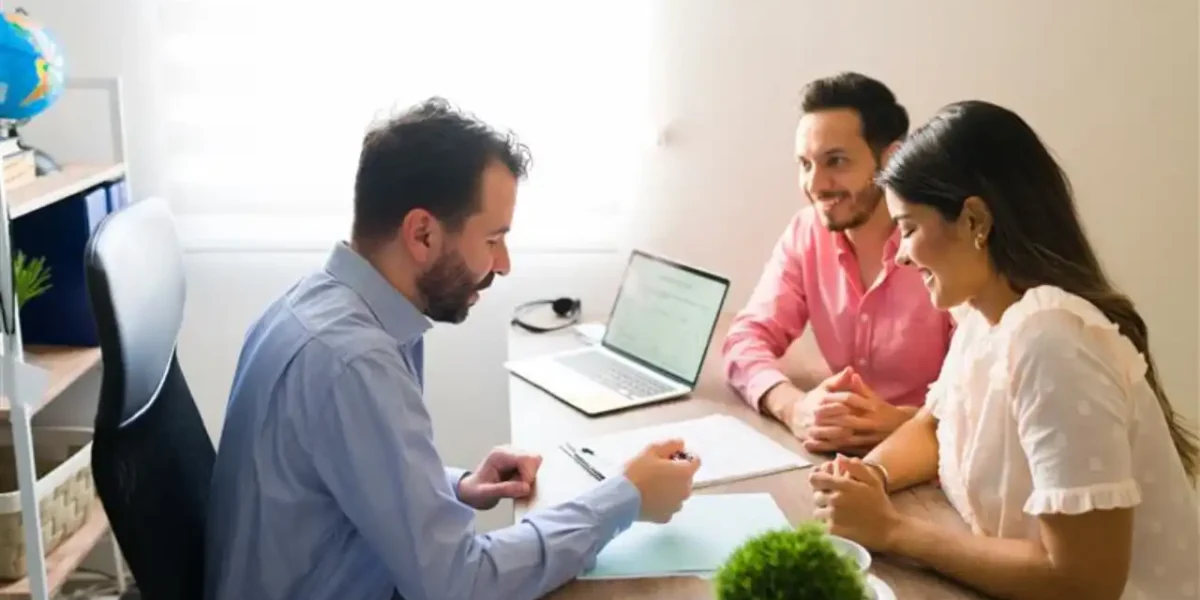 A couple is consulting with a lawyer while reviewing and discussing a legal agreement document in an office.