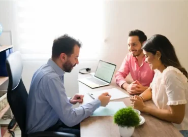 A couple is consulting with a lawyer while reviewing and discussing a legal agreement document in an office.